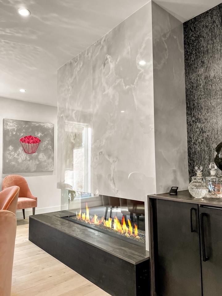 Three sided glass linear fireplace with light stone slab surround and dark stone hearth